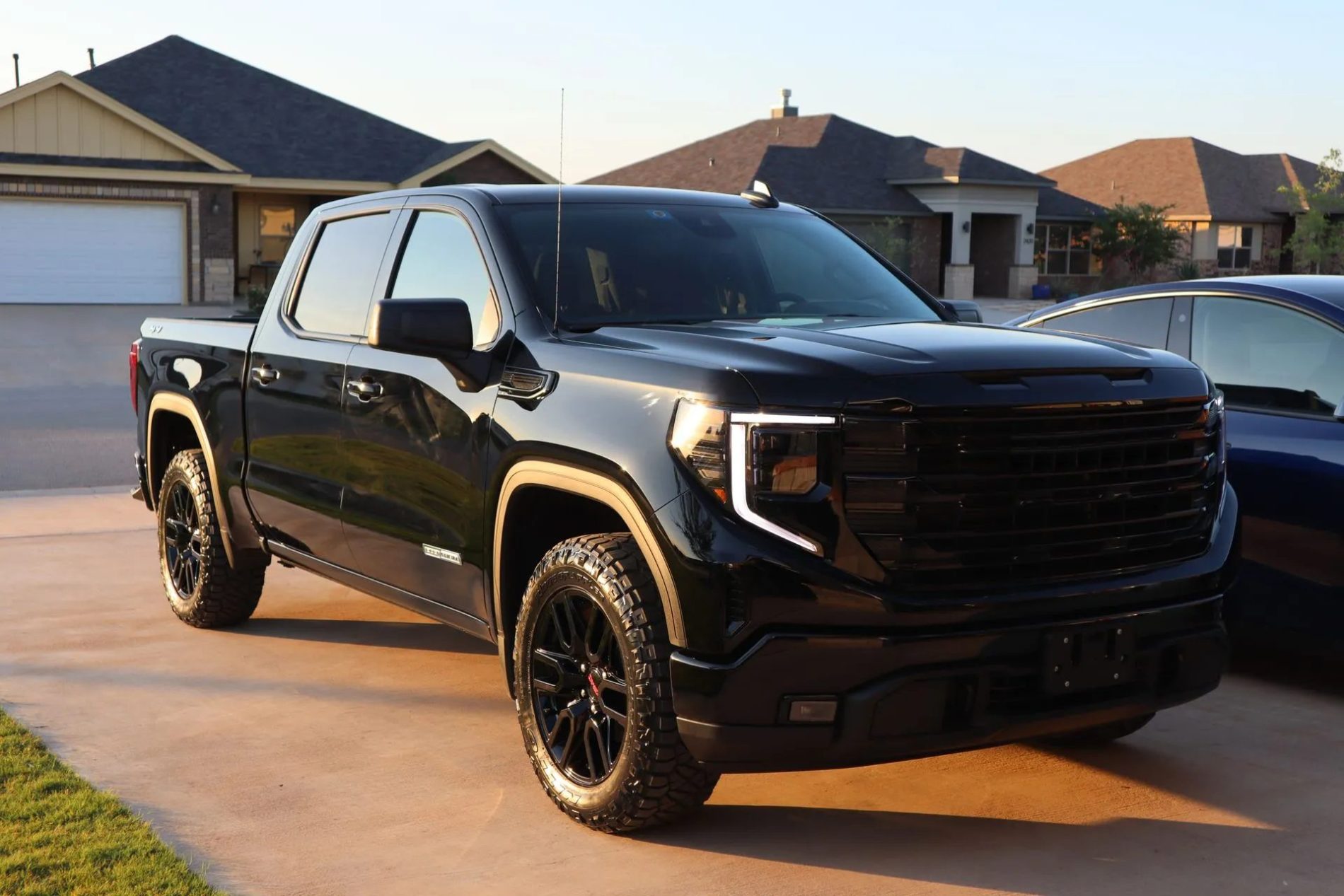 A black pickup truck is parked in a residential driveway with houses visible in the background.