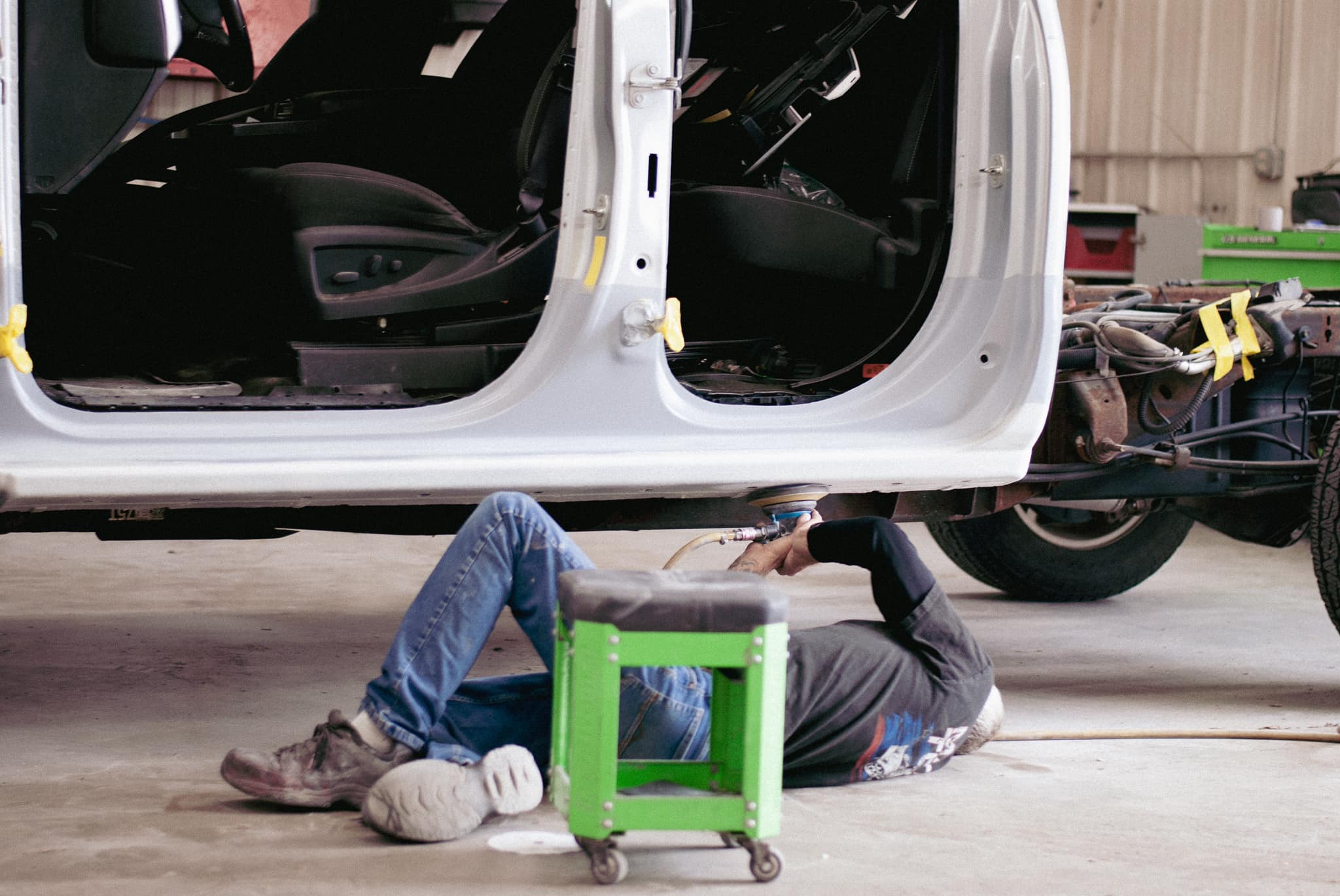 ASE-certified technicians A person lies on the floor under a vehicle, working with tools in an auto repair shop.